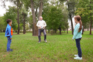 Naklejka na ściany i meble Senior man and his grandchildren playing with ball in park