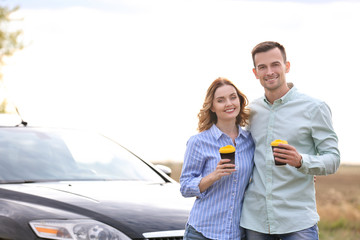 Beautiful young couple with coffee standing near car