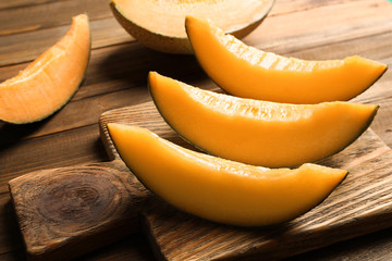 Cutting board with sliced melon on wooden background