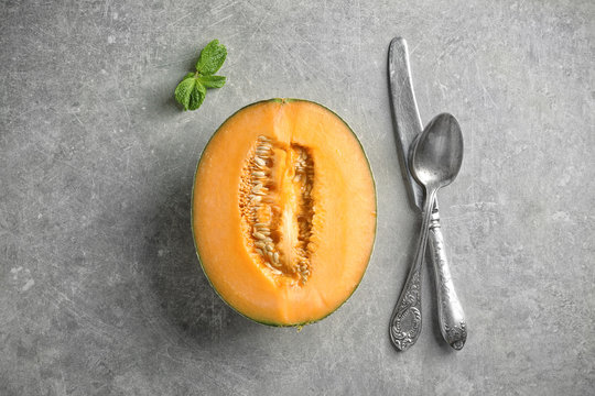 Half of fresh melon with knife and spoon on grey background