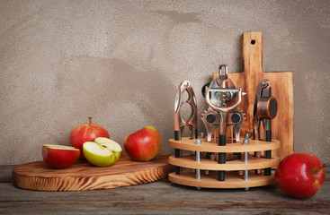 Stand with kitchen utensils and apples on table against wall