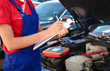 Young female mechanic with clipboard near car in body shop