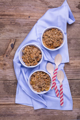 Apple crumble served in individual ramekins placed on top of a kitchen towel. Wooden background. 