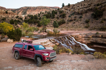 Red pickup camping rig on rocky trail near waterfall in southern Utah