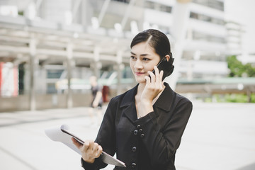 Business woman with document in hand talking on cell phone near business center