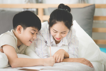 Happy Asian brother and sister rest on the bed and writing.