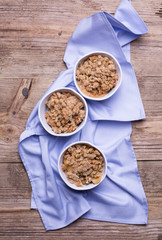 Homemade crumble served in individual ramekins. Linen napkin is placed underneath the ramekins. Rustic wooden background 