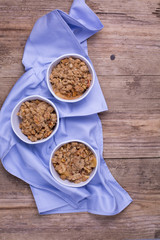 Apple crumble served in white ramekins. Cotton blue napkin placed under the dishes. Rustic wooden background 