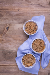 Apple crumble served in individual white ramekins placed on top of a blue cotton napkin. Rustic wood background. Copy space. 