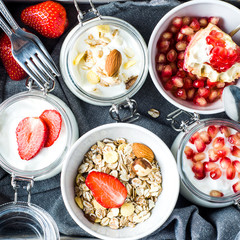 Yogurt in glass jars, dry mix, pomegranate and strawberries in a wooden box