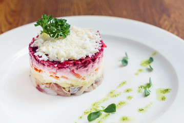 layered salad with herring, beets, carrots, onions, potatoes and eggs close-up on a plate