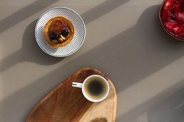 A white cup of espresso with milk on a wooden background and cakes with nuts and strawberries on a saucer on a gray background.