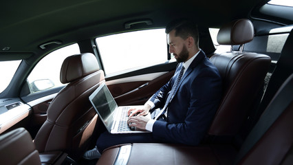 Fototapeta na wymiar businessman using a laptop in the backseat of a car