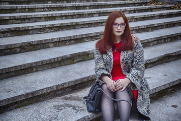 Sad or tired or thoughtful woman in leopard coat sitting on the concrete stairway and think about her life