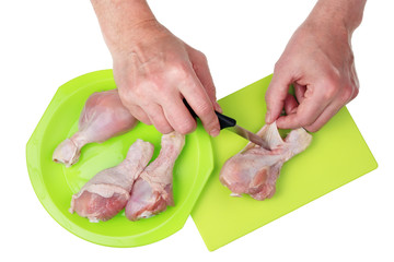 On a plastic kitchen cutting board, an old chef with his hands  and knife separates fat skin from  chicken legs.