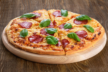 Pepperoni pizza with salami and basil on dark wooden background.