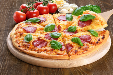 Pepperoni pizza with salami and basil on dark wooden background.