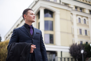 A young serious man in a suit is holding a coat and looking away.