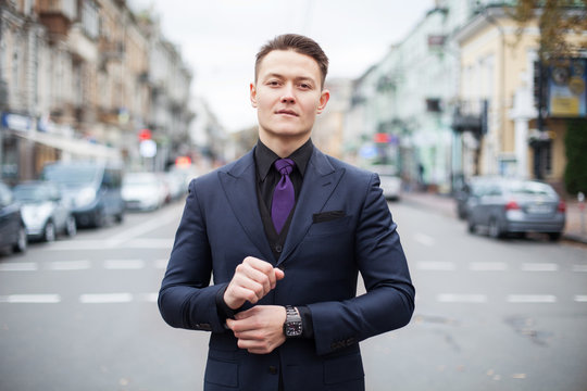 Portrait of a young serious professional. Dressed in a blue slim suit and black shirt, a young handsome businessman stands on a busy street in a big city.