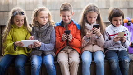 girls and boy with smartphones on bench in park