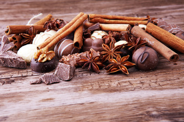A selection of assorted chocolate truffle pralines on a wooden table with dark chocolate, cinnamon and anise.
