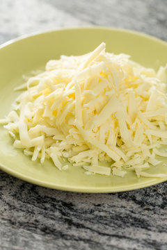 Grated cheese pile on the plate above grey granite background