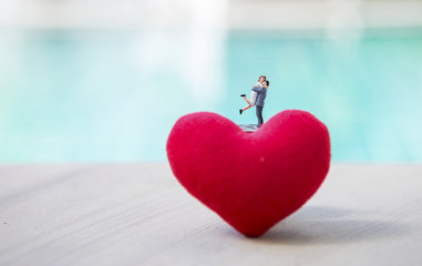 Miniature happy couple on red heart over blurred blue background, Valentine concept background