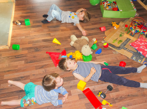 Children lie on the floor among the toys. The children made the mess and lay down on the floor..