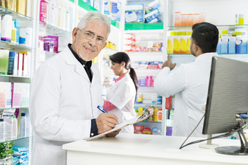 Obraz premium Senior Chemist Writing On Clipboard While Coworkers Working In P