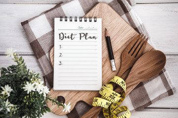 Line Notepad with Diet Plan list text  on chopping board with wooden fork and spoon and the  measuring tape on white table , recipes food or diet plan for healthy habits shot note background concept - obrazy, fototapety, plakaty