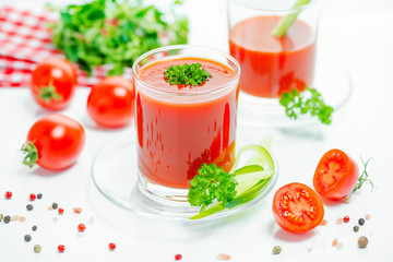 red tomato juice in transparent glasses with parsley, cutted tomato fruit, cucumber and dry pepper, close up