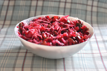 Vinaigrette salad in the white bowl on the checkered fabric background close-up