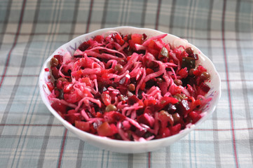 Vinaigrette salad in the white bowl on the checkered fabric background close-up