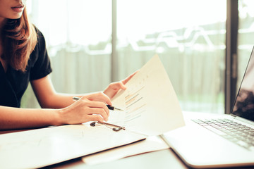 Business woman working at office with laptop and documents,rear view of young business woman hands busy using holding documents,Open space loft office reading sitting at the desk on office.