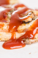 Closeup macro of pizza slice with ham mushrooms and ketchup on the white marble