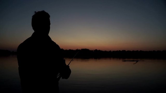 Silhouette fisherman throwing fishing rod in river on background evening sunset