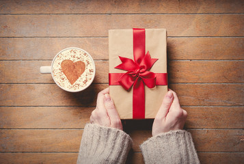 Female hands holding gift box and cup of coffee