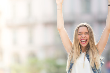 Cheerful teenager outdoor, gesturing with her hands. Defocused background with copy space.