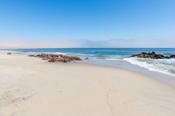 Fototapeta na wymiar Sandy beach and coast line on the Atlantic ocean at Cape Cross, Namibia, famous for the nearby seal colony. Clear blue sky.