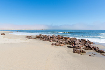 Fototapeta na wymiar Sandy beach and coast line on the Atlantic ocean at Cape Cross, Namibia, famous for the nearby seal colony. Clear blue sky.