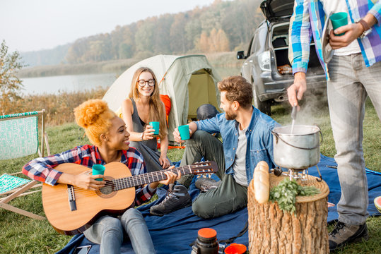 Multi ethnic group of friends dressed casually clinking glasses during the dinner outdoors at the camping - Powered by Adobe