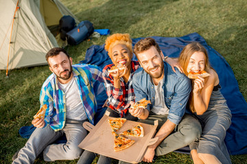 Multi ethnic group of firends dressed casually having fun eating pizza during the outdoor...