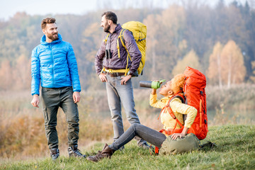 Group of friends in colorful jackets having a break with backpacks outdoors on the green lawn