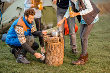 Friends heating fondue to have a dinner during the outdoor recreation at the camping in the evening
