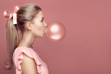 Beautiful blonde woman blowing gum. Fashion portrait on pink background.