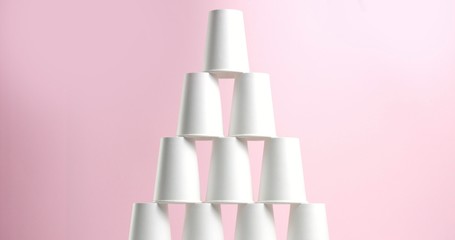 Tower made of white paper cups on pink background