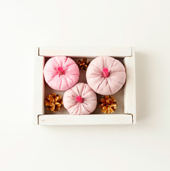 Pink pumpkins and golden pine cones in wooden box