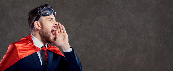 A businessman in a superhero costume calls screams on the background of space for text.