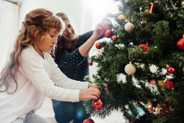 Mother and daughter decorating Christmas tree.