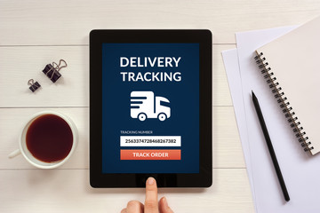 Delivery tracking concept on tablet screen with office objects on white wooden table. All screen content is designed by me. Flat lay
